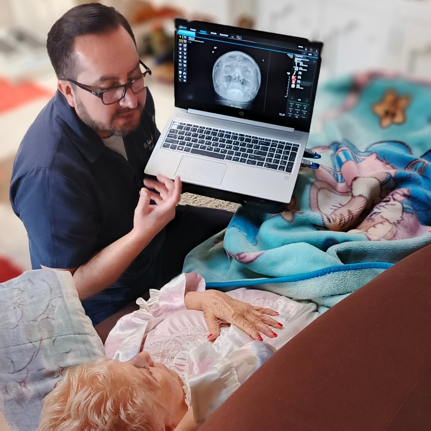Tecnólogo mostrando radiografía en laptop a paciente adulta mayor en cama